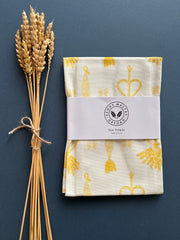 White tea towel with a bright yellow print of traditional corn dolly emblems