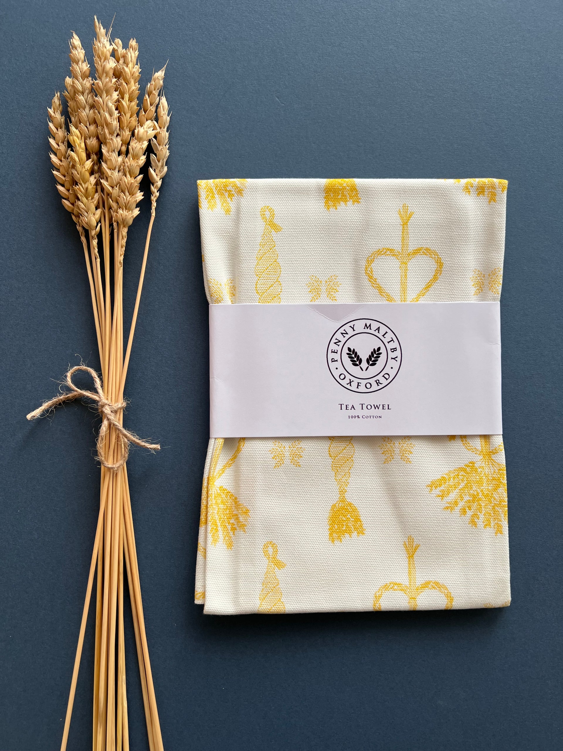 White tea towel with a bright yellow print of traditional corn dolly emblems