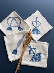 Set of four square white napkins printed with corn dolly images in blue, each napkins shows a different design of corn dolly.