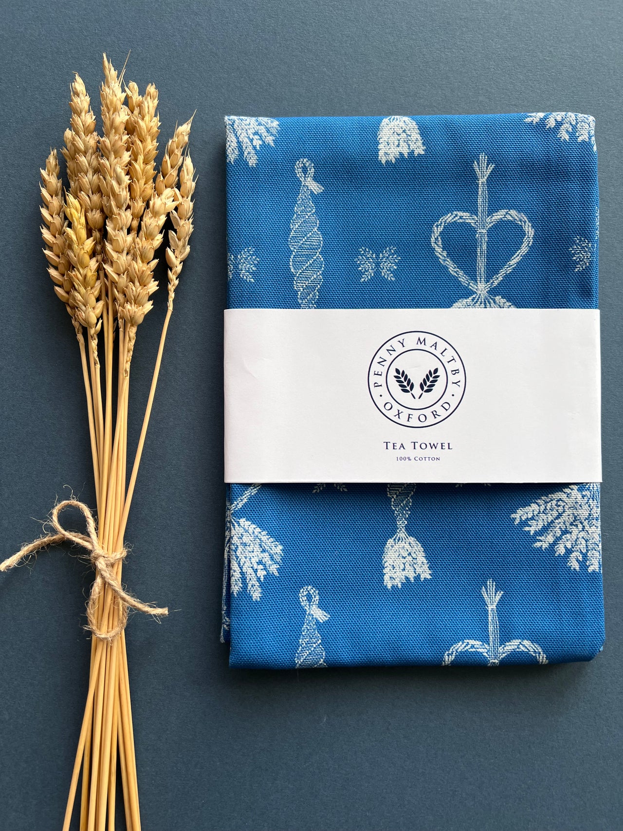 Indigo blue tea towel depicting white corn dolly pattern.