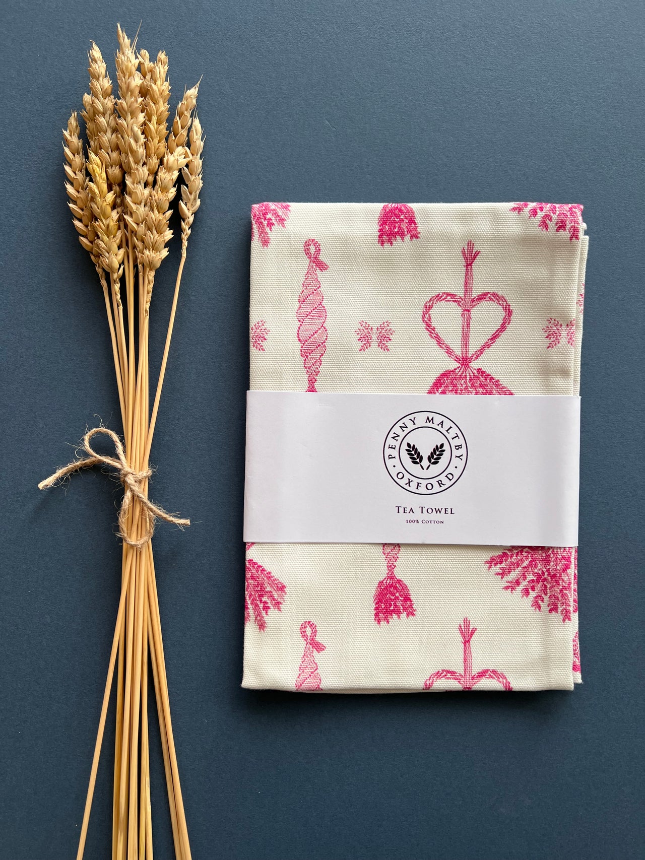 White tea towel with original corn dolly pattern in pink by Penny Maltby