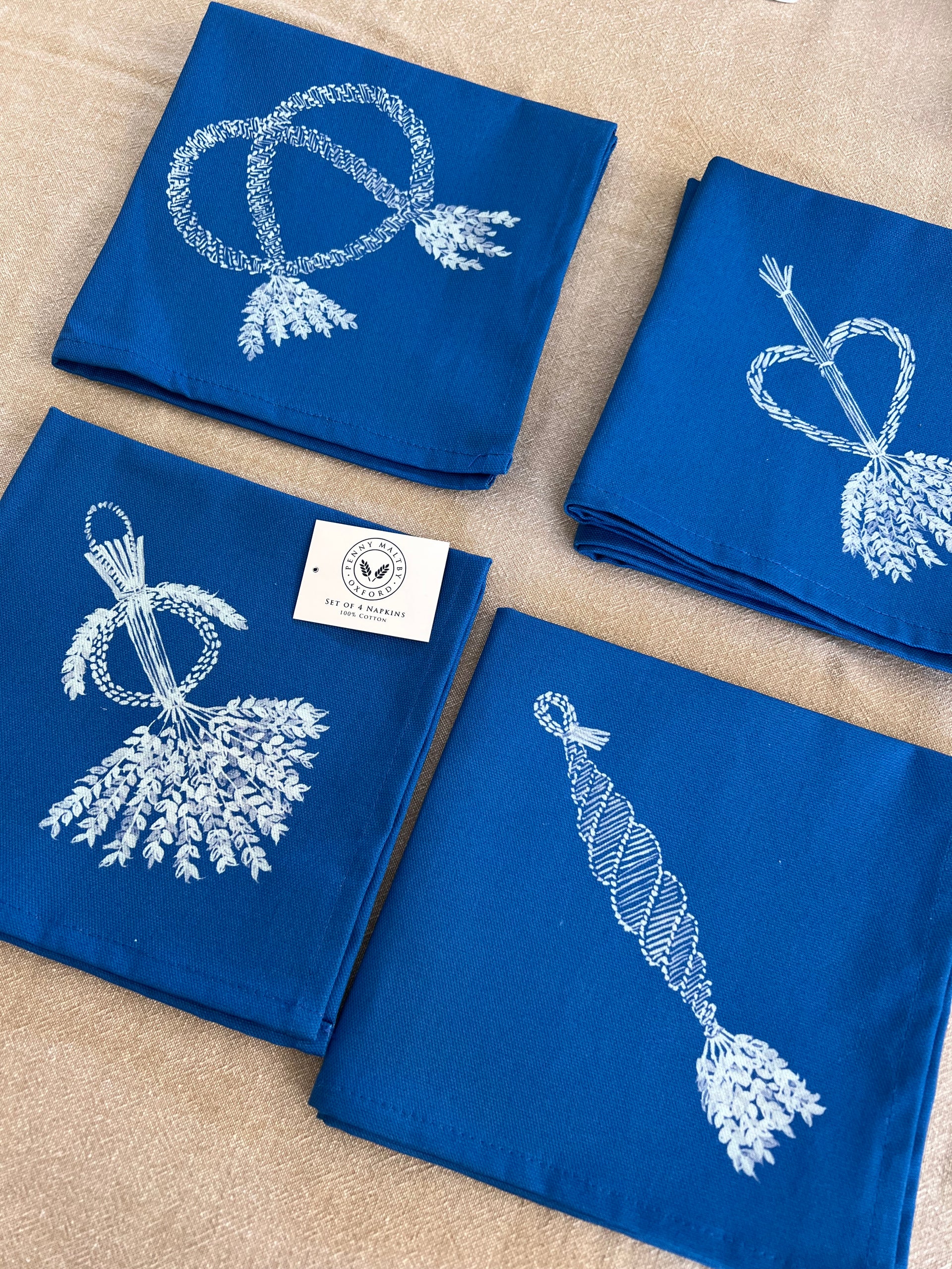 Set of four cotton napkins in indigo cotton with four different corn dolly patterns printed in white.